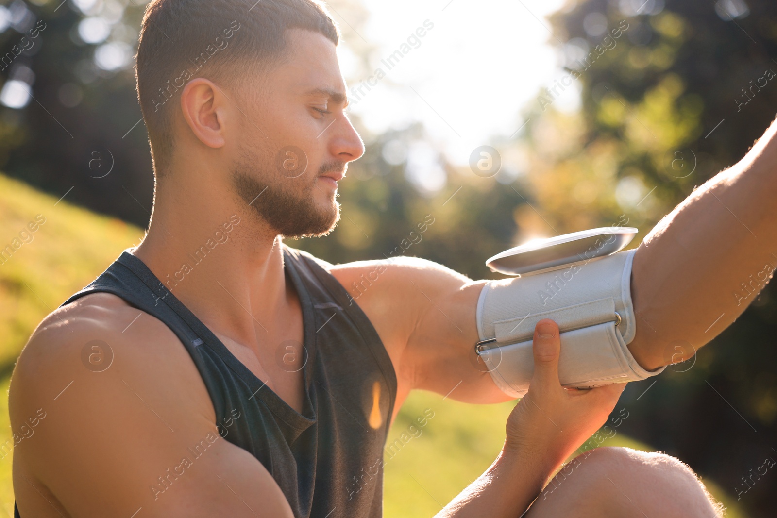 Photo of Attractive serious man checking blood pressure with modern monitor after training in park