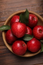 Photo of Ripe red apples and green leaves in bowl on wooden table, top view