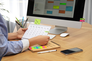 Photo of Woman making schedule using calendar at table in office, closeup