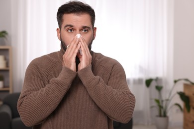 Sick man with tissue blowing nose at home, space for text. Cold symptoms