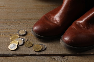 Photo of Poverty. Old boots and coins on wooden table, closeup