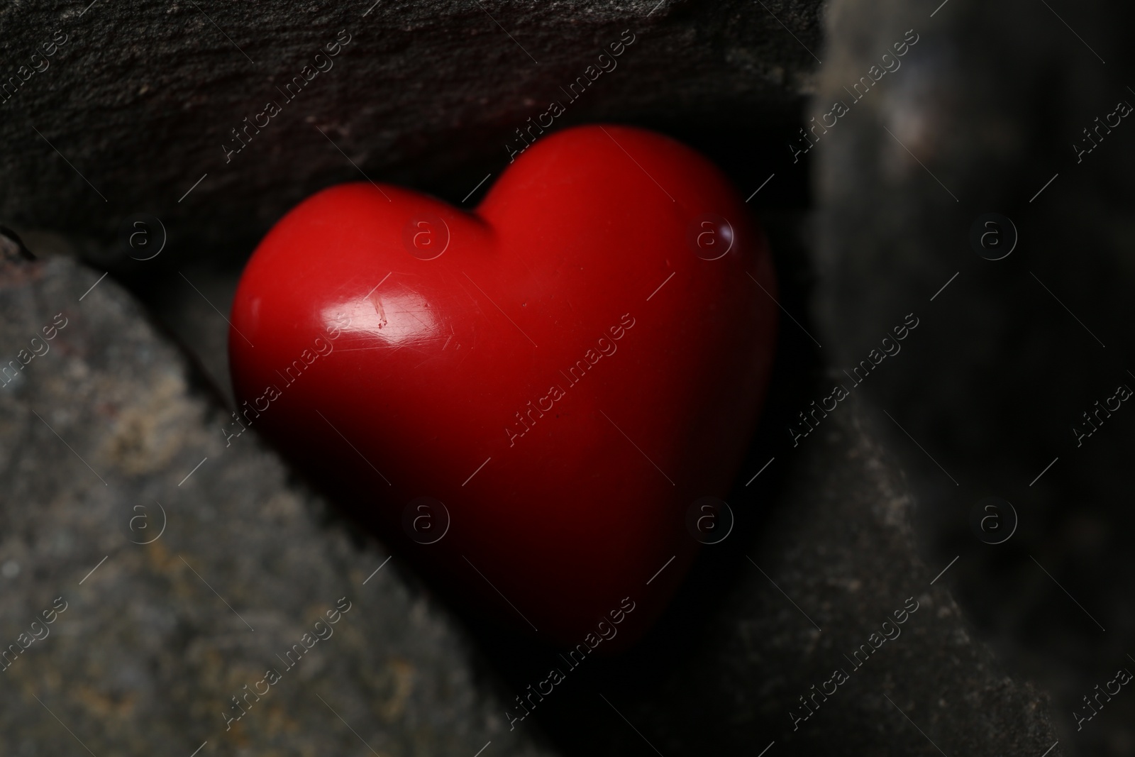 Photo of One red decorative heart between stones, closeup
