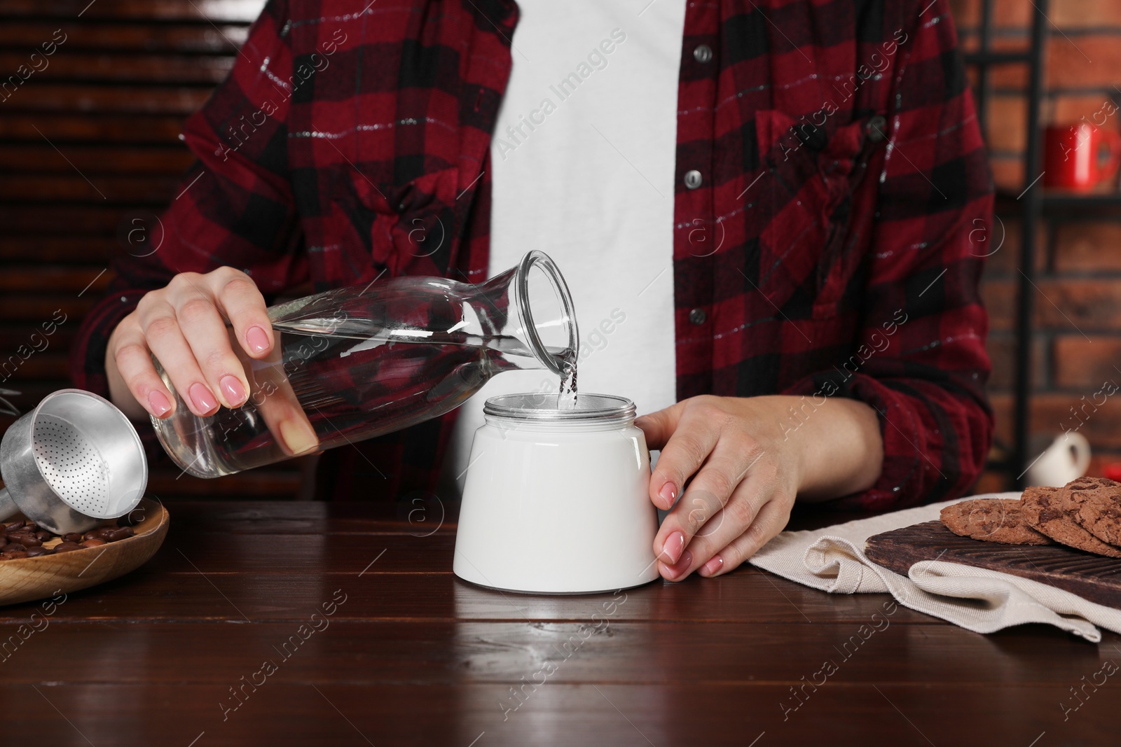 Photo of Brewing coffee. Woman pouring water into moka pot at wooden table indoors, closeup