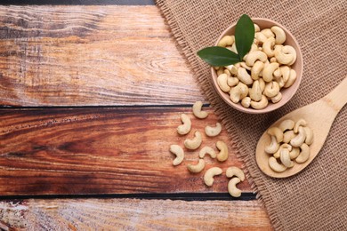 Photo of Tasty cashew nuts and green leaves on wooden table, flat lay. Space for text