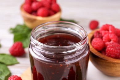 Glass jar of delicious raspberry jam on table, closeup