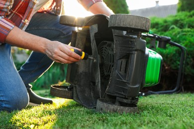Photo of Man with screwdriver fixing lawn mower in garden, closeup