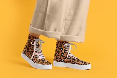 Photo of Woman wearing classic old school sneakers with leopard print on orange background, closeup