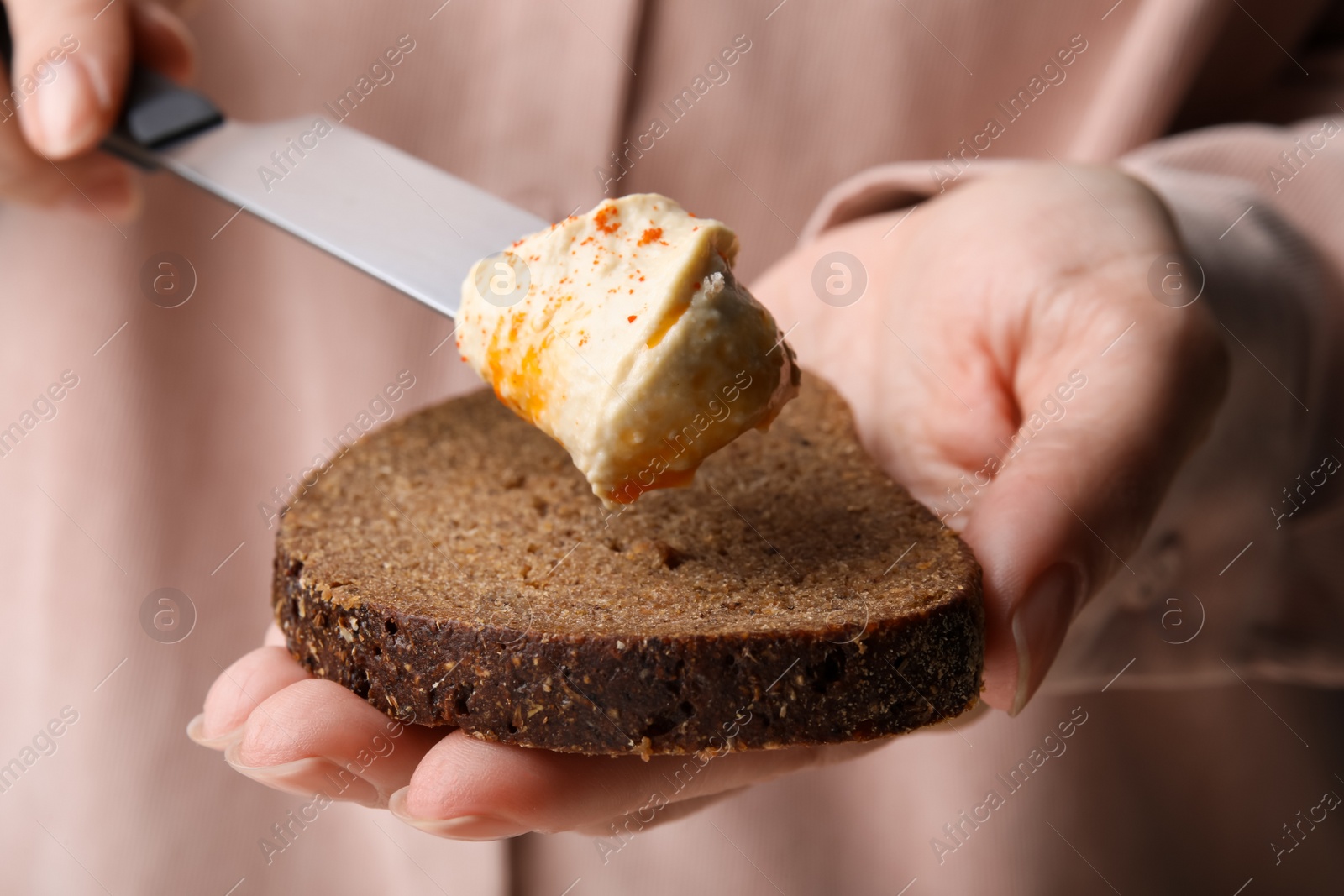 Photo of Woman spreading delicious hummus onto bread, closeup