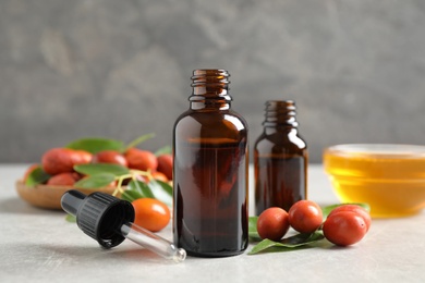 Photo of Glass bottles with jojoba oil and seeds on stone table against grey background