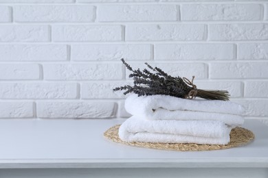 Photo of Clean towels and beautiful lavender flowers on white table against brick wall, space for text