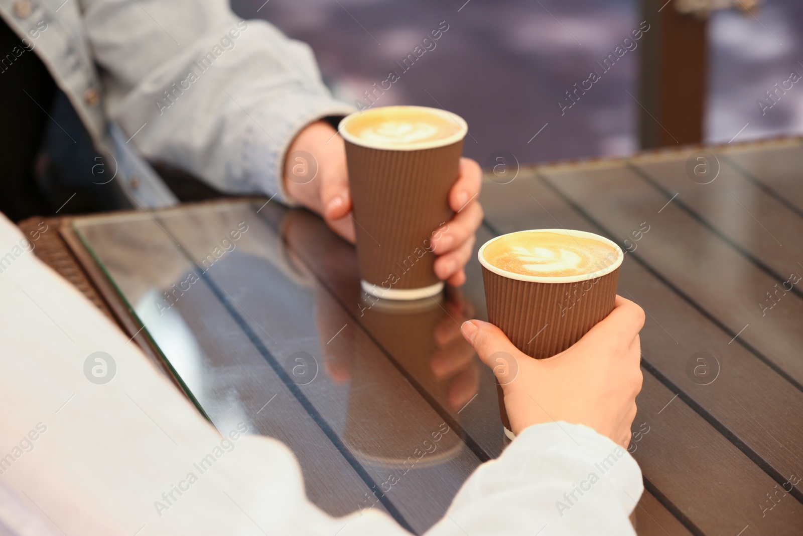 Photo of Women holding takeaway paper cups at table, closeup. Coffee to go