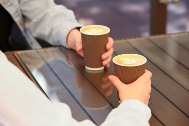 Women holding takeaway paper cups at table, closeup. Coffee to go