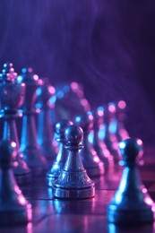 Photo of Chess pieces on checkerboard in color light, selective focus