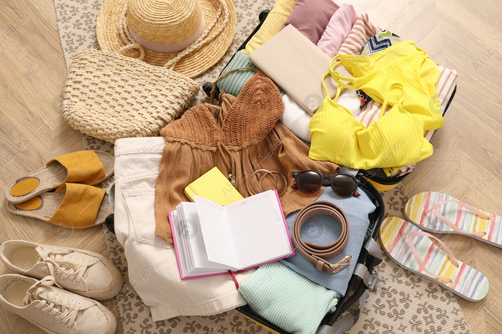 Photo of Open suitcase with clothes, shoes and summer accessories on wooden floor, top view