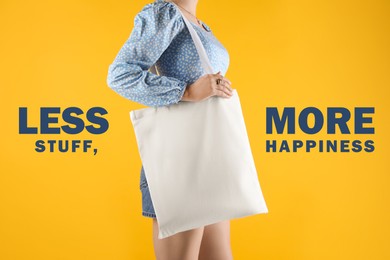 Less stuff more happiness, affirmation. Woman holding textile bag on yellow background, closeup