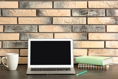 Photo of Modern laptop on table against brick wall. Mock up with space for text
