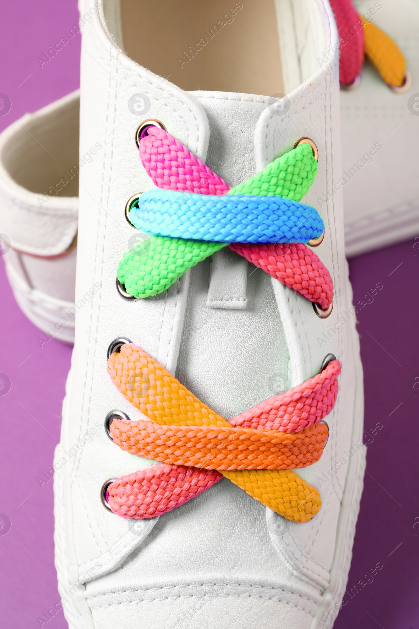 Image of Stylish sneakers with rainbow shoe laces on purple background, closeup