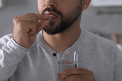 Man with glass of water taking antidepressant pill on blurred background, closeup