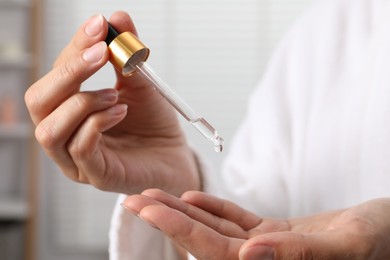 Woman applying cosmetic serum onto her hand on blurred background, closeup