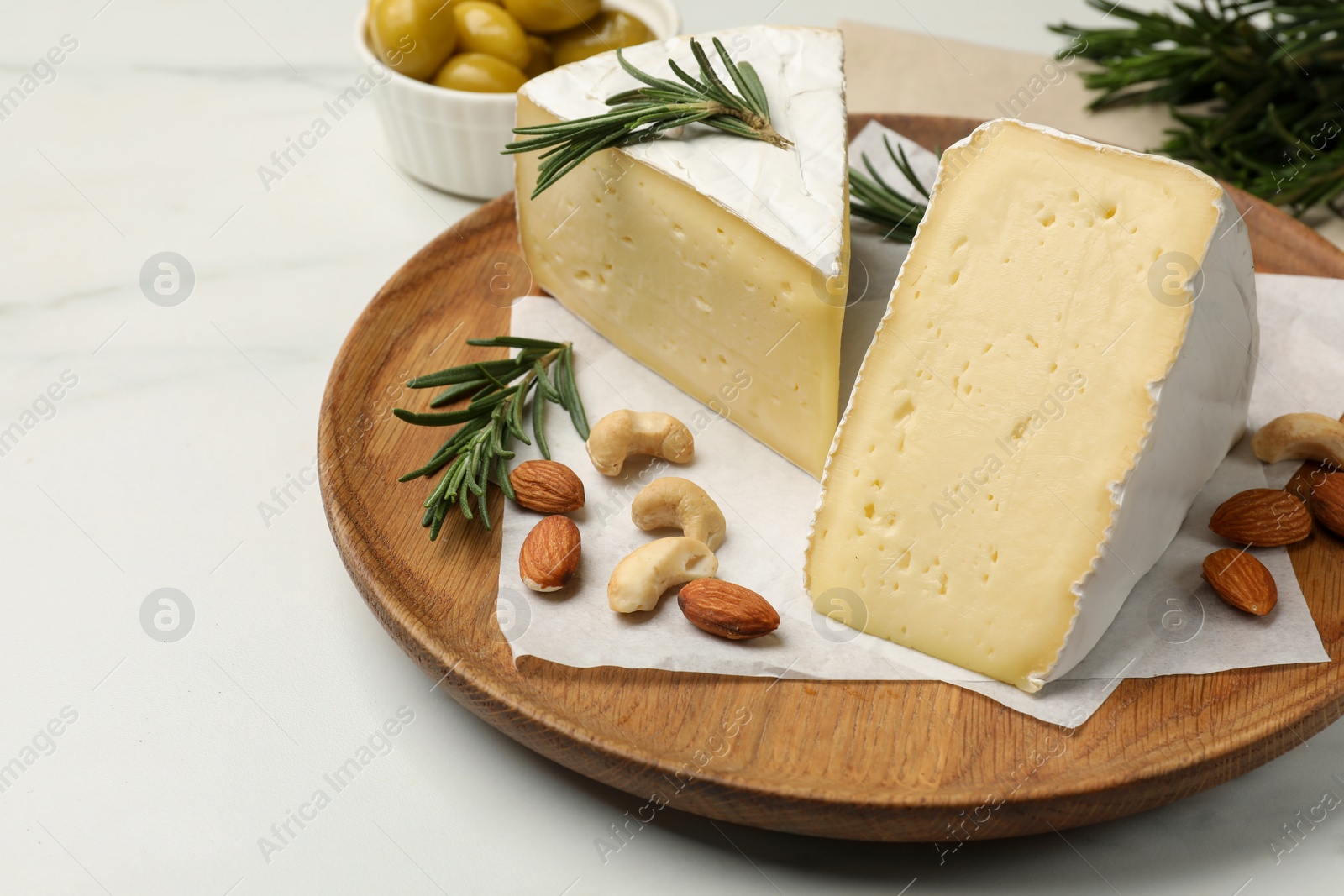 Photo of Plate with pieces of tasty camembert cheese, nuts and rosemary on white table, closeup. Space for text