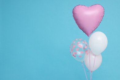 Photo of Bunch of heart and round shaped balloons on light blue background, space for text. Birthday party