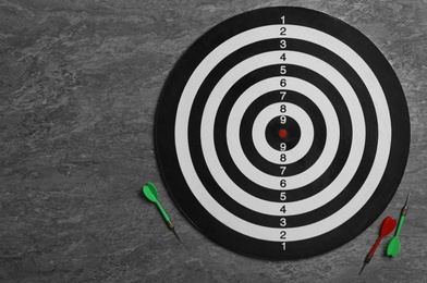 Photo of Dart board with color arrows on grey stone background, top view. Space for text