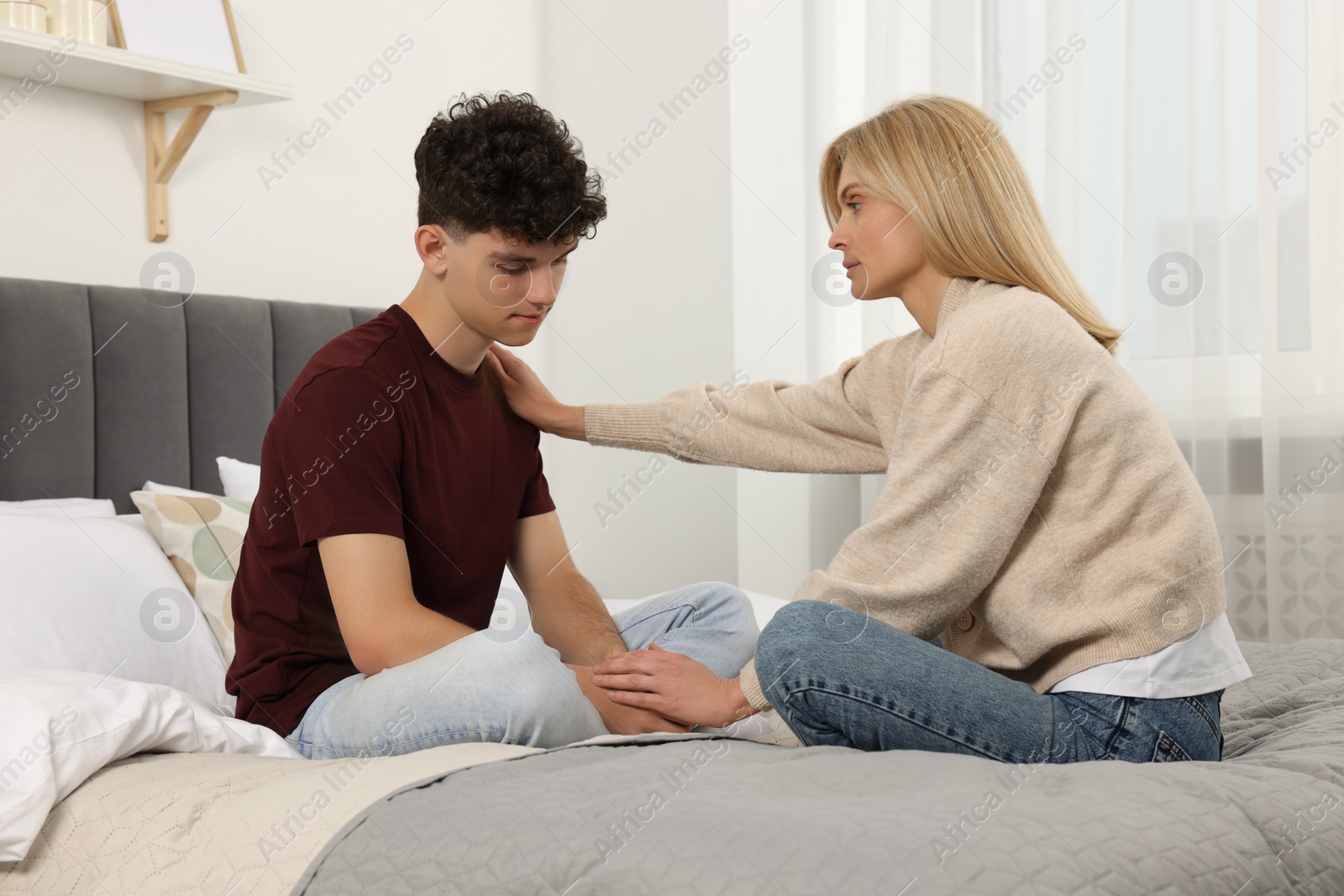 Photo of Mother consoling her upset son in bedroom. Teenager problems