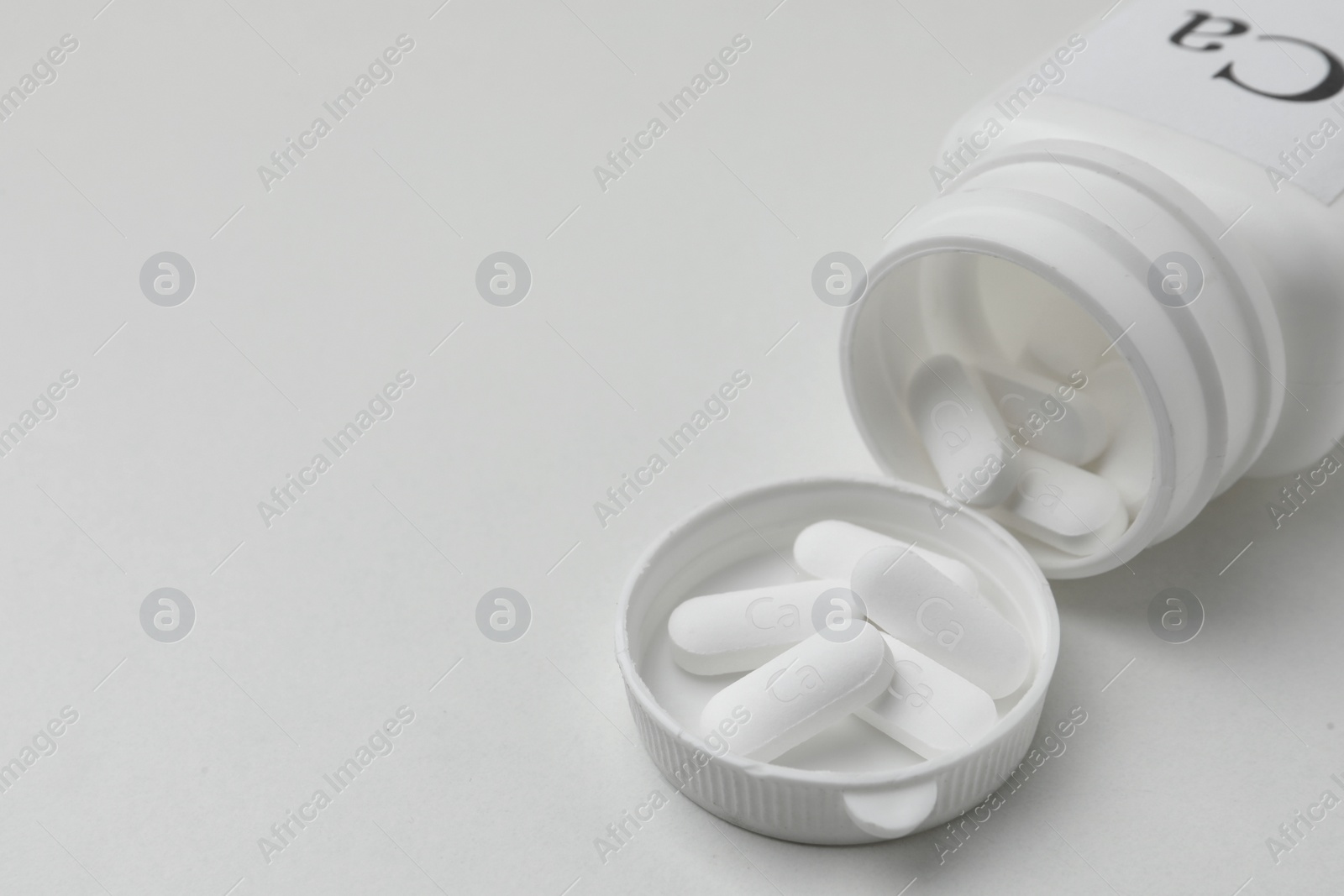 Photo of Overturned jar of calcium supplement pills on white background, closeup. Space for text