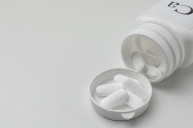 Photo of Overturned jar of calcium supplement pills on white background, closeup. Space for text
