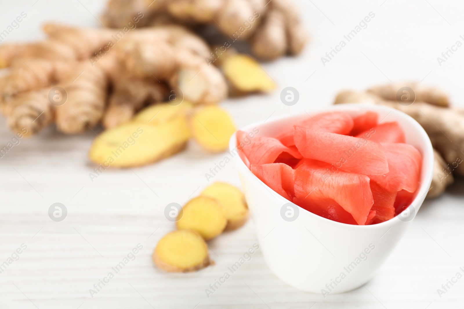 Photo of Spicy pickled ginger and root on white wooden table, closeup. Space for text