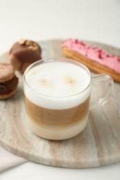 Aromatic coffee in cup, tasty macarons and eclair on white table