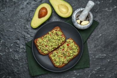 Photo of Slices of bread with tasty guacamole and avocado on black textured table, flat lay