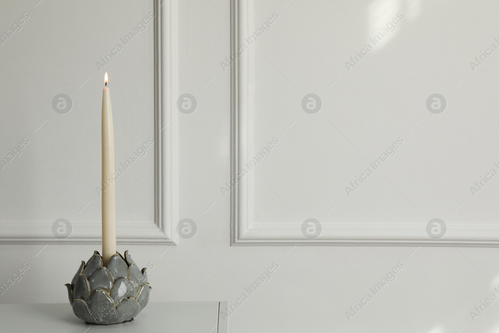 Photo of Holder with burning candle on table near white wall indoors, space for text