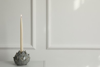 Holder with burning candle on table near white wall indoors, space for text