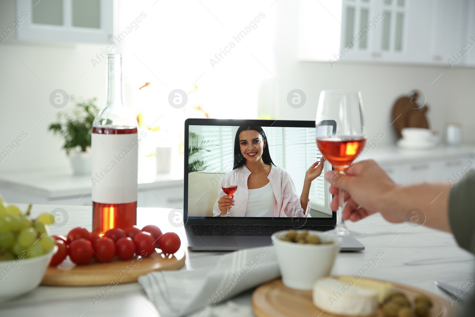 Photo of Friends drinking wine while communicating through online video conference in kitchen. Social distancing during coronavirus pandemic