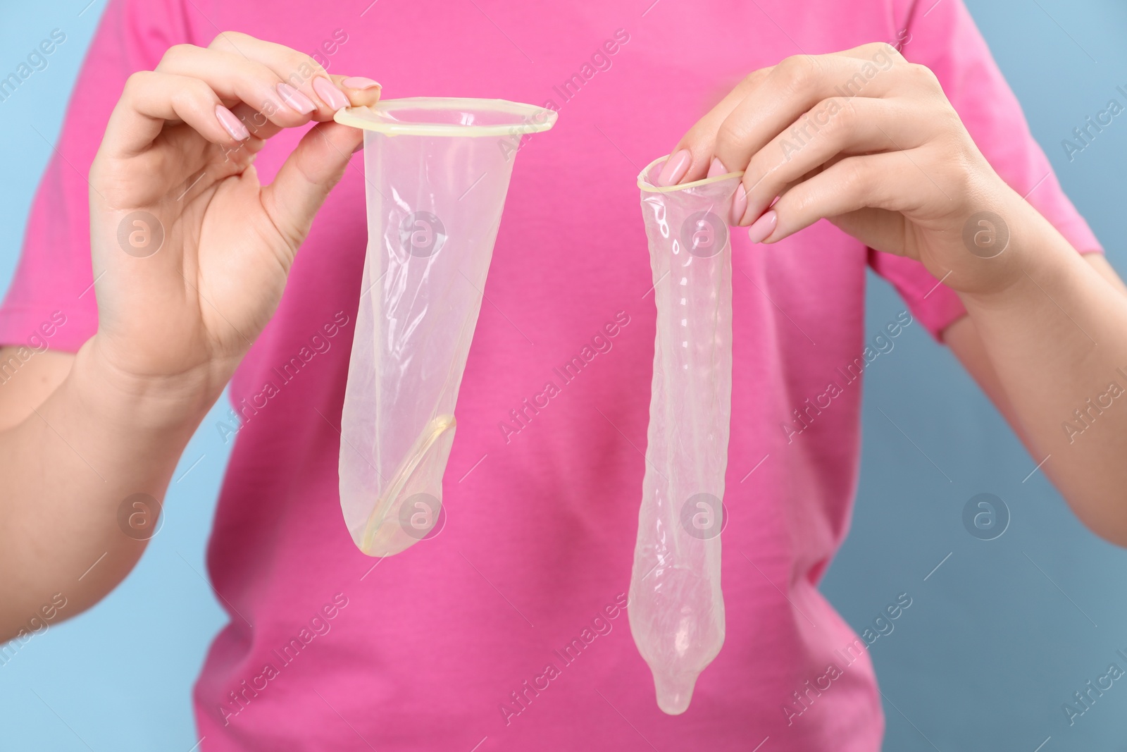 Photo of Woman with unrolled female and male condoms on light blue background, closeup. Safe sex