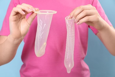 Woman with unrolled female and male condoms on light blue background, closeup. Safe sex