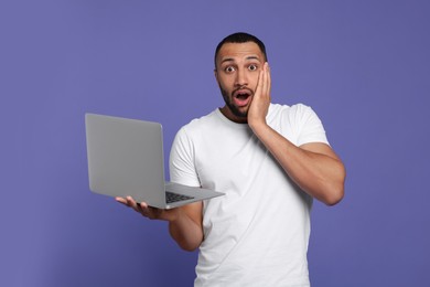 Surprised young man with laptop on lilac background