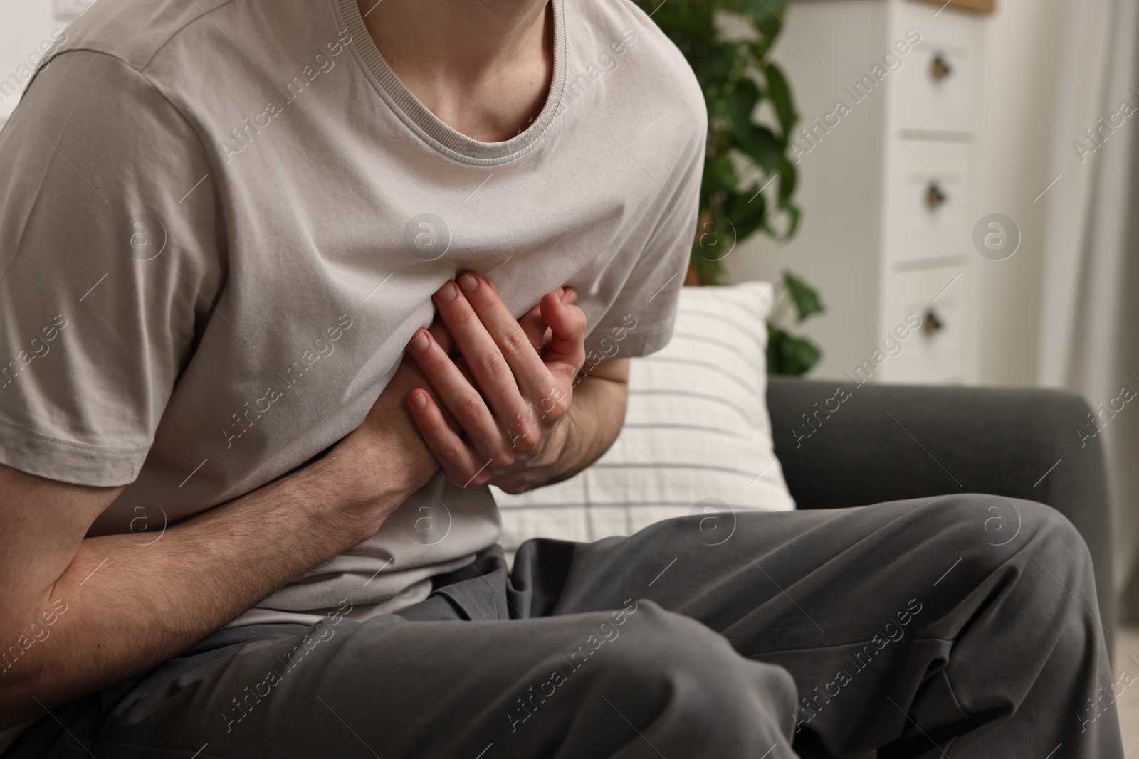 Photo of Man suffering from heart hurt on sofa at home, closeup