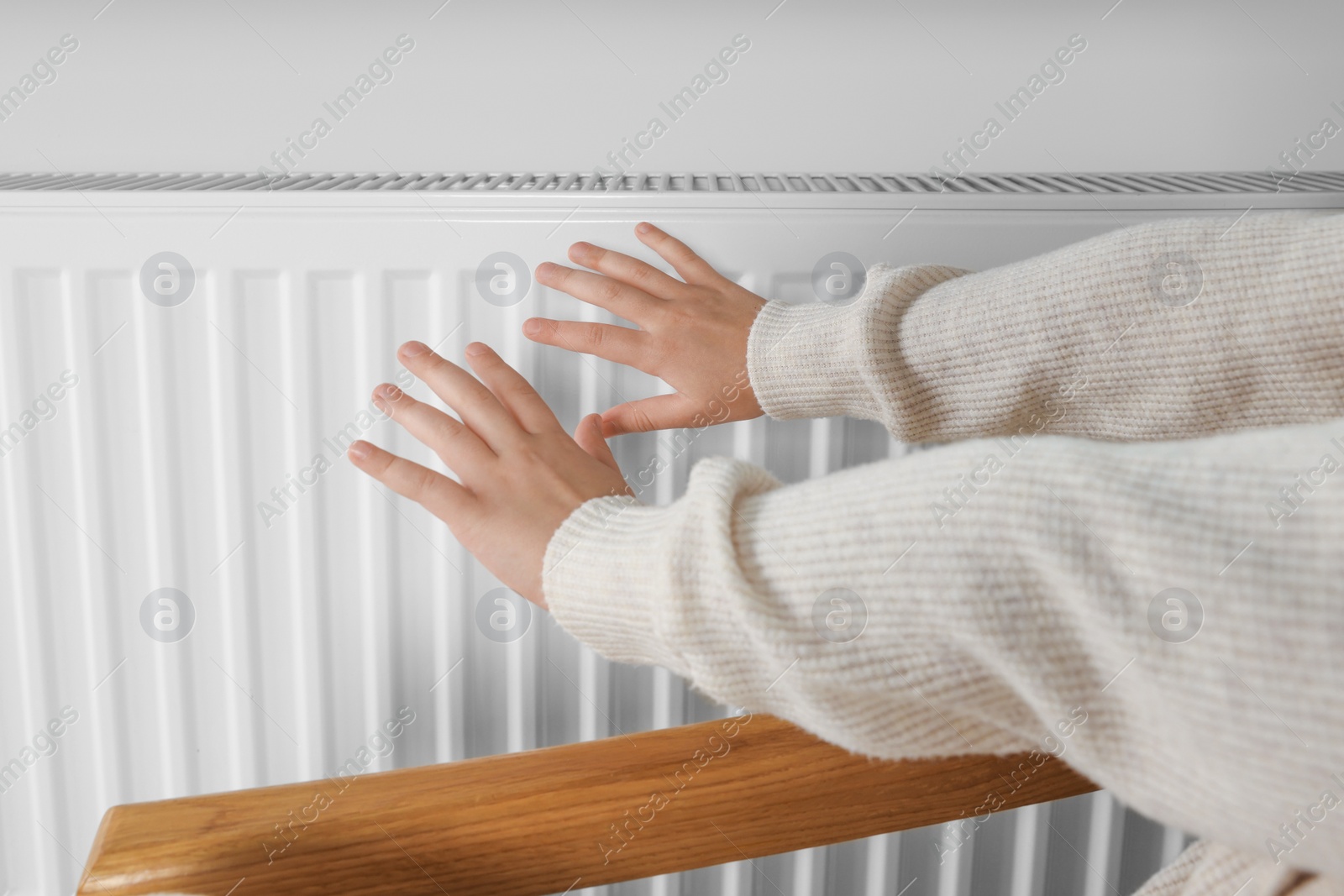 Photo of Little girl warming hands near heating radiator indoors, closeup