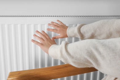 Photo of Little girl warming hands near heating radiator indoors, closeup