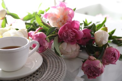 Beautiful peonies and cup of tea on table, closeup