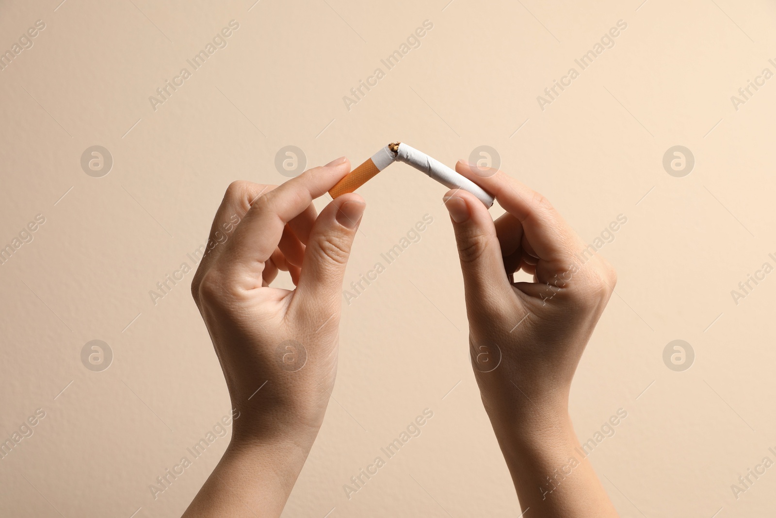 Photo of Stop smoking. Woman holding broken cigarette on beige background, closeup