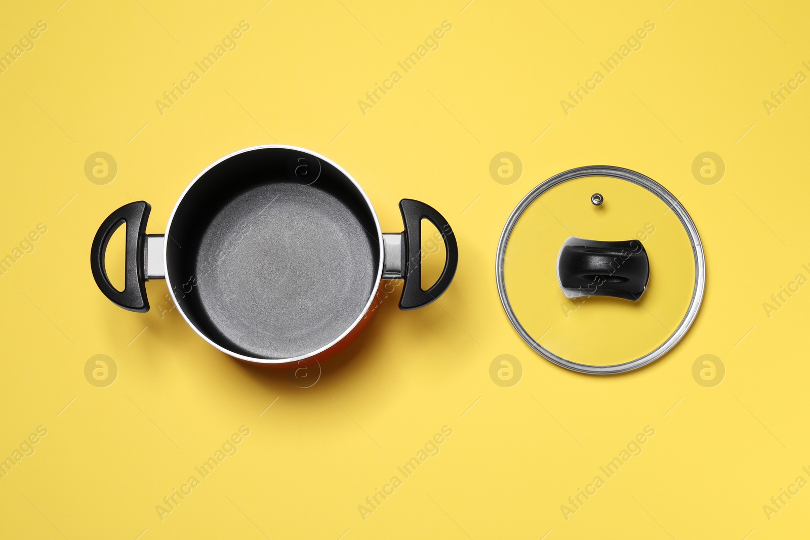 Photo of Empty pot and glass lid on yellow background, flat lay