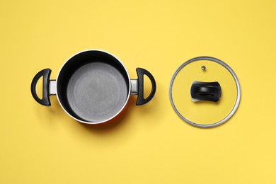 Empty pot and glass lid on yellow background, flat lay