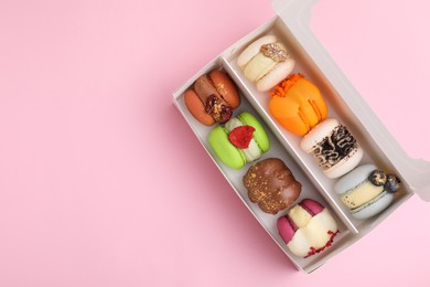 Cardboard box with delicious macarons on pink table, top view. Space for text