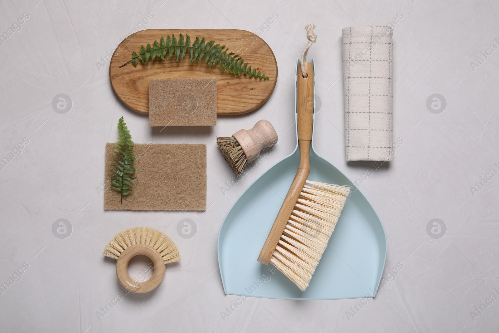 Photo of Cleaning brushes, scoop, sponges, towel and fern leaves on light grey background, flat lay