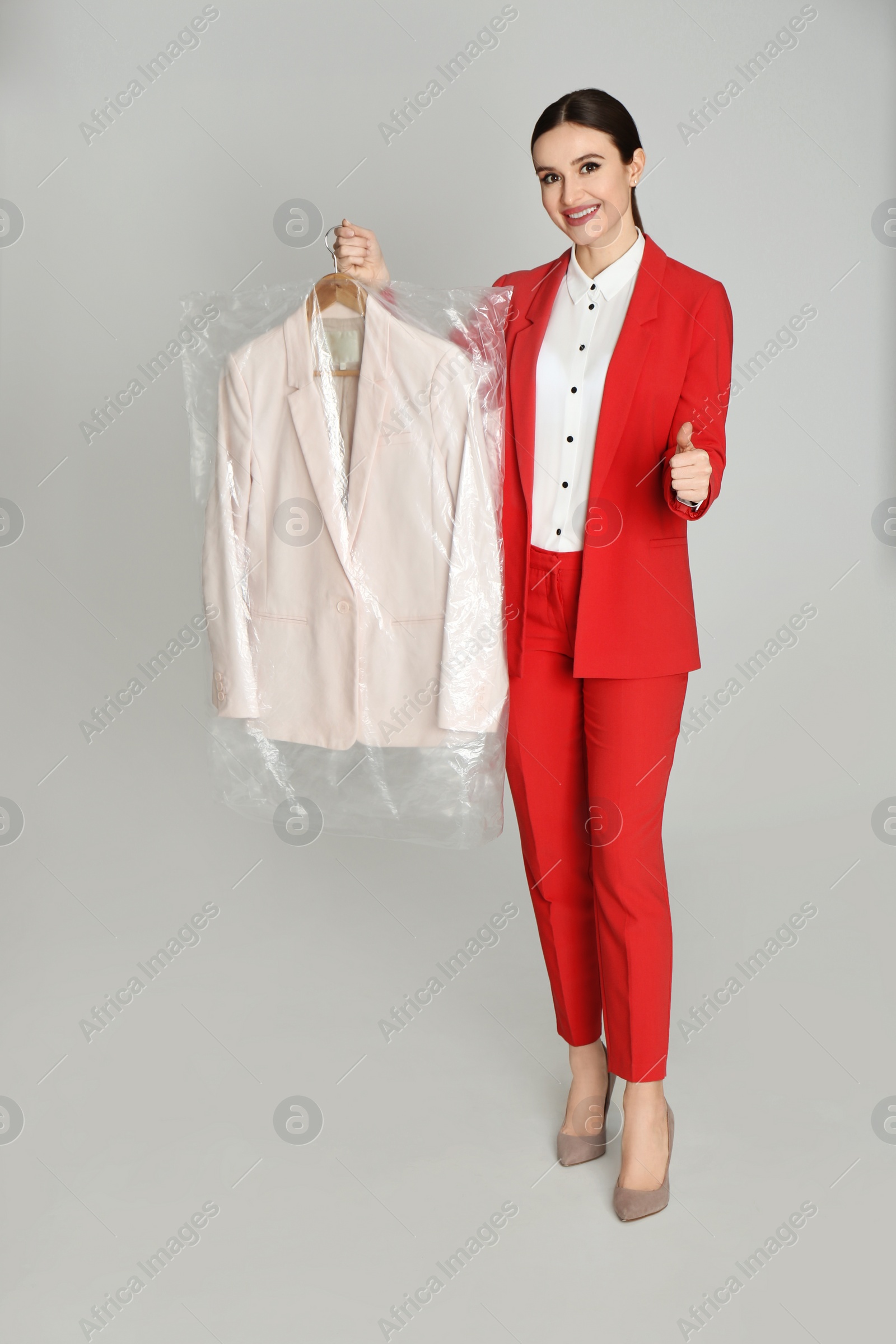 Photo of Young woman holding hanger with jacket on light grey background. Dry-cleaning service
