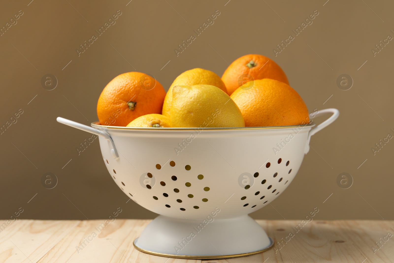 Photo of Colander with fresh citrus fruits on wooden table