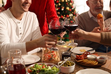 Photo of Happy family clinking glasses of wine at festive dinner, focus on hands. Christmas celebration